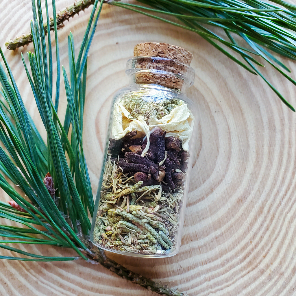 Small glass bottle filled with dried herbs on a wooden surface with green leaves.