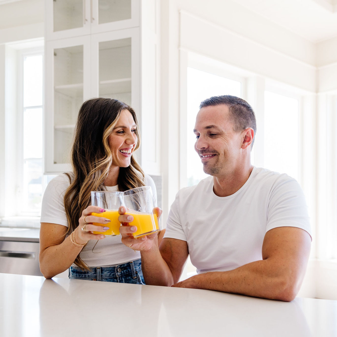 Man and woman sitting at a kitchen counter with orange juice glasses.