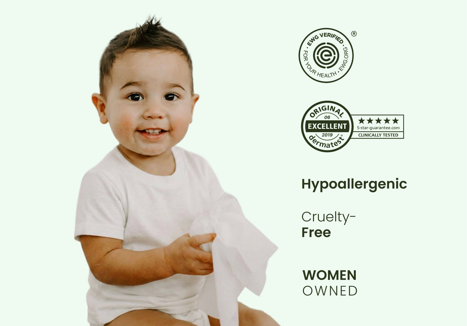 Smiling baby in a white shirt and diaper holding a soft baby wipe beside hypoallergenic, dermatologist-tested, cruelty-free, and women-owned certification logos on a light green background.
