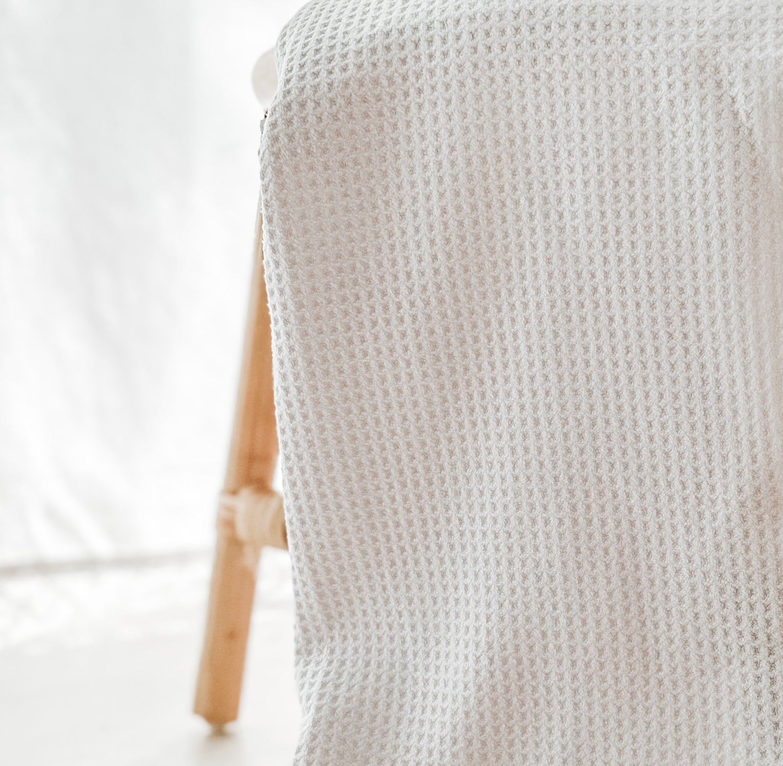 Close-up of a soft white waffle-weave kitchen tea towel featuring a textured absorbent fabric, draped over a natural wooden chair.