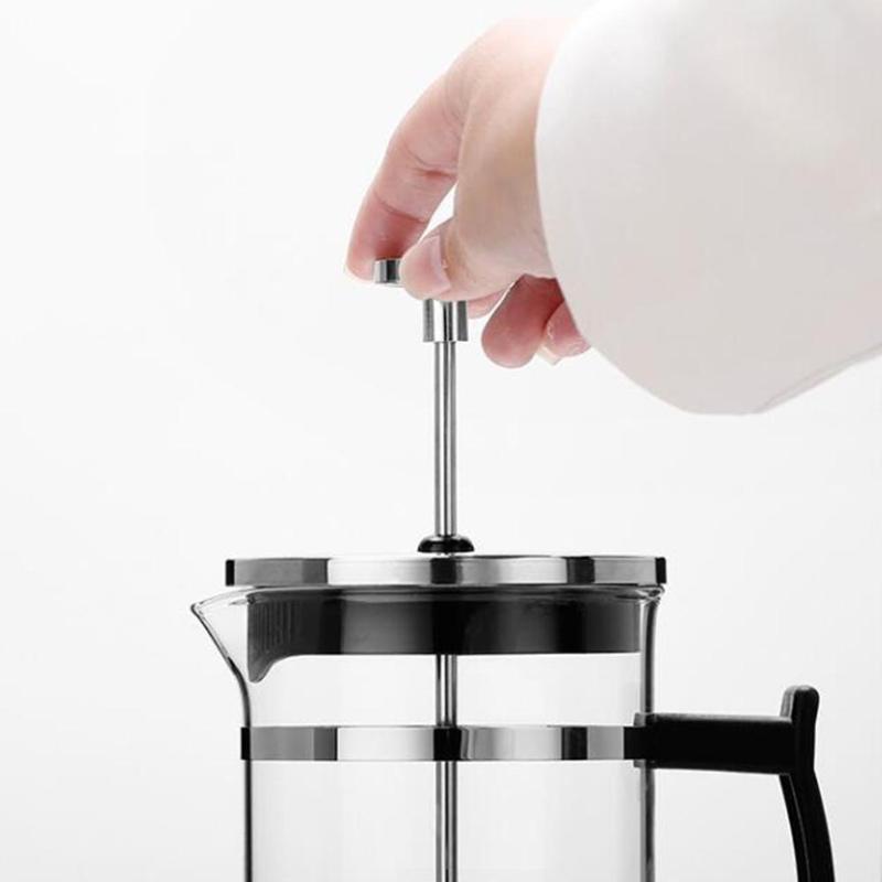 Hand pressing the plunger of a heat-resistant glass French press coffee maker with stainless steel filter and black handle for rich home-brewed coffee