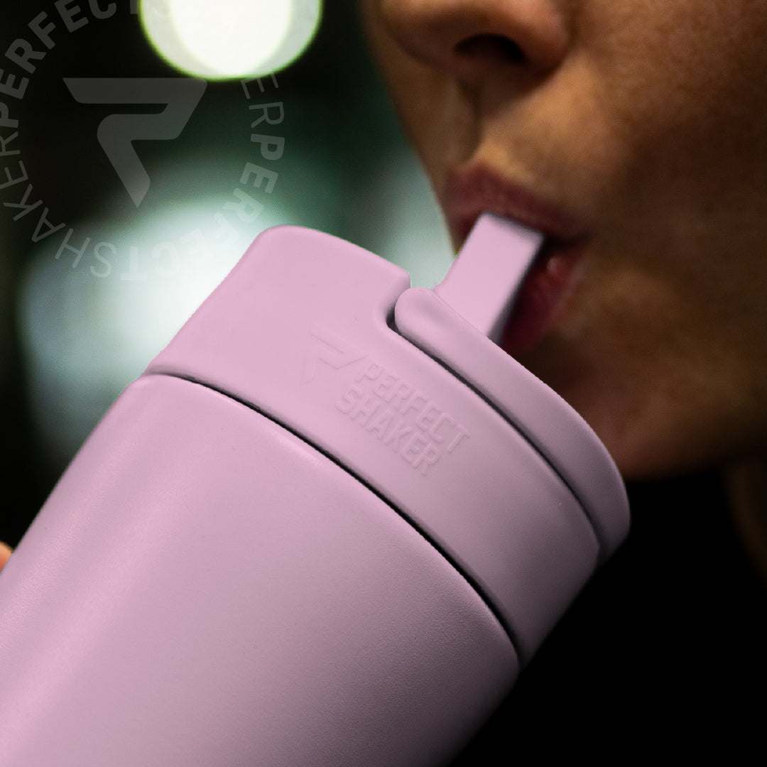 A close-up lifestyle shot of a person drinking from a matte light purple insulated tumbler with a matching straw lid. The brand name 'PERFECT SHAKER' is embossed on the lid.