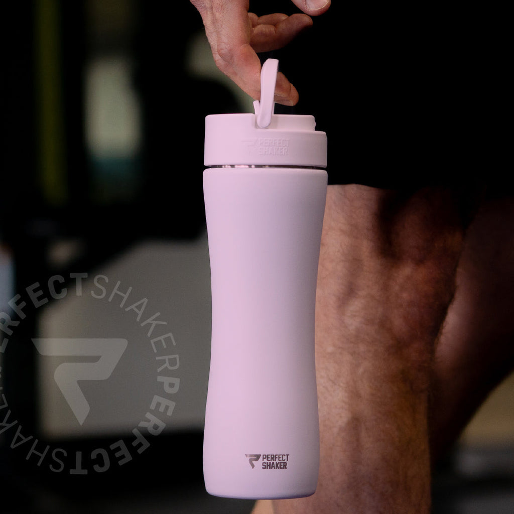 A light pink insulated water bottle with a flip-top lid being held by a person in a gym setting. The brand name 'PERFECT SHAKER' is visible near the bottom of the bottle.