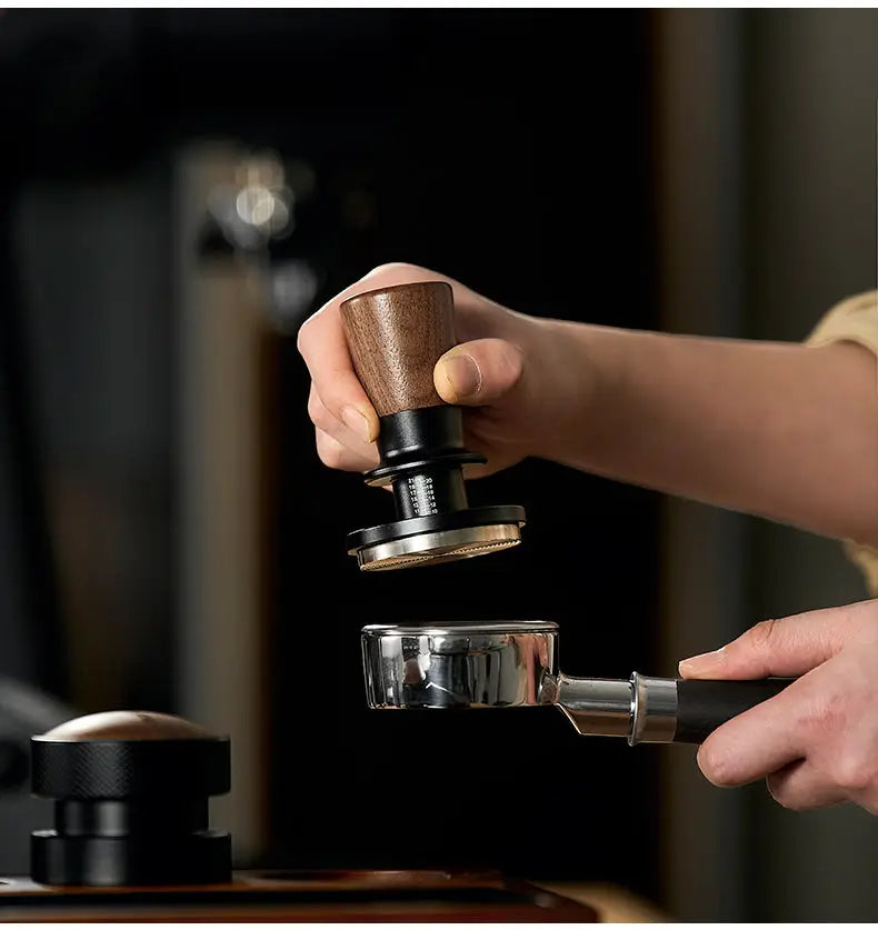 Muyu constant force spring espresso tamper with walnut wood handle and stainless steel base tamping coffee grounds in a portafilter for consistent espresso extraction