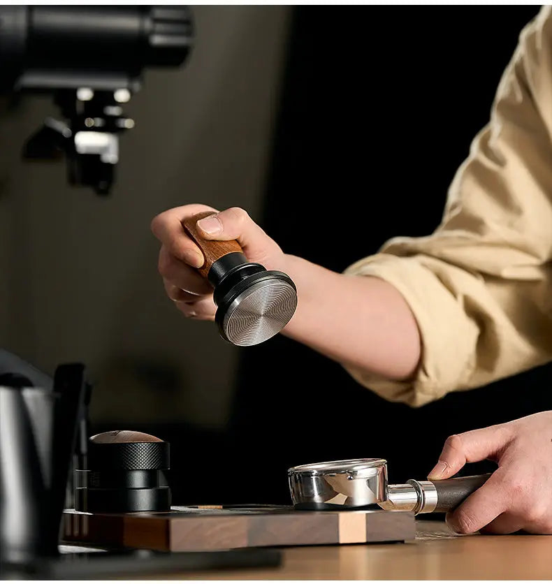 Barista using a Muyu constant force spring espresso tamper with walnut wood handle and stainless steel base to evenly compress coffee grounds in a portafilter for consistent espresso extraction.