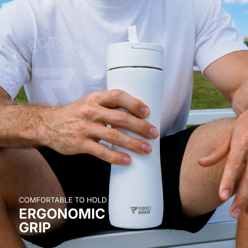 Person holding a white tumbler with ergonomic grip, sitting outdoors.