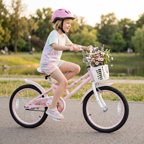 A young child wearing a pink helmet rides a pink children's bicycle with a white front basket filled with flowers on a paved path in a park at sunset.