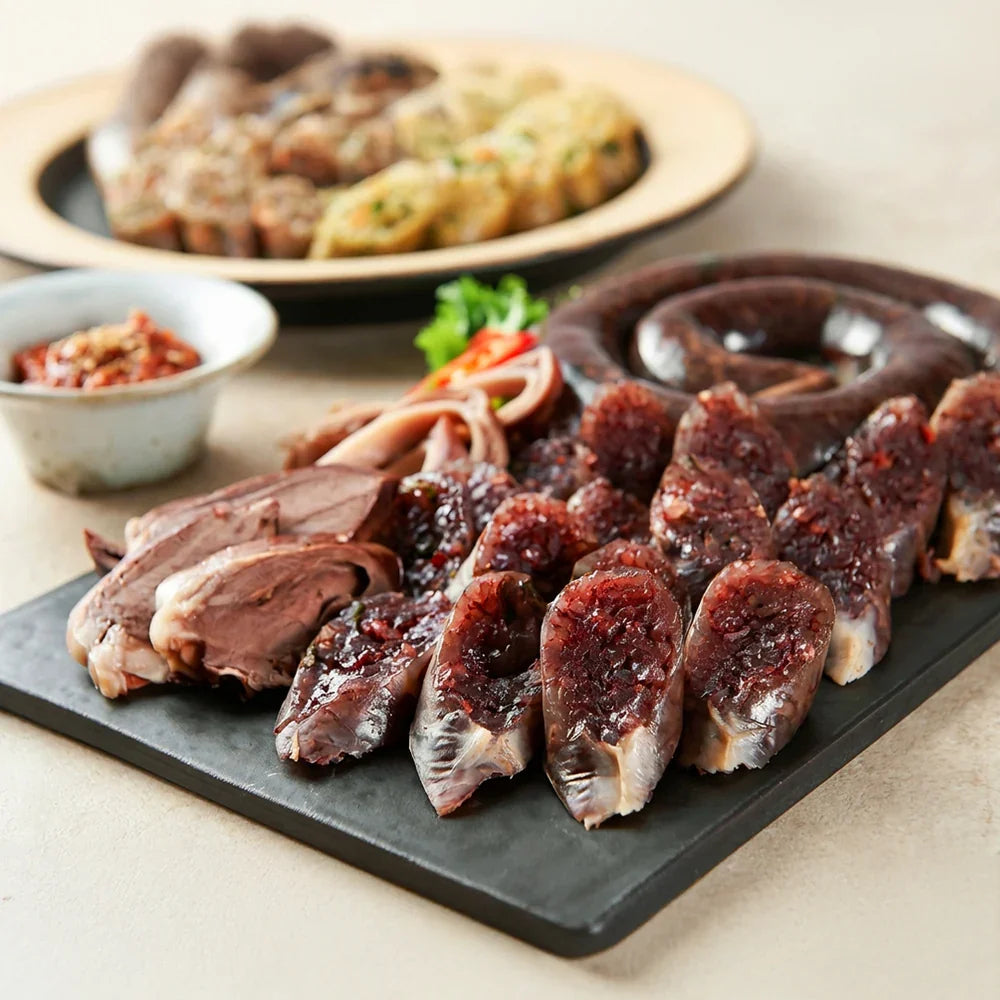 Plated Korean blood sausage (sundae) with sliced glutinous rice sausage, pork offal, dipping sauce, and traditional Korean side dishes on a serving platter.
