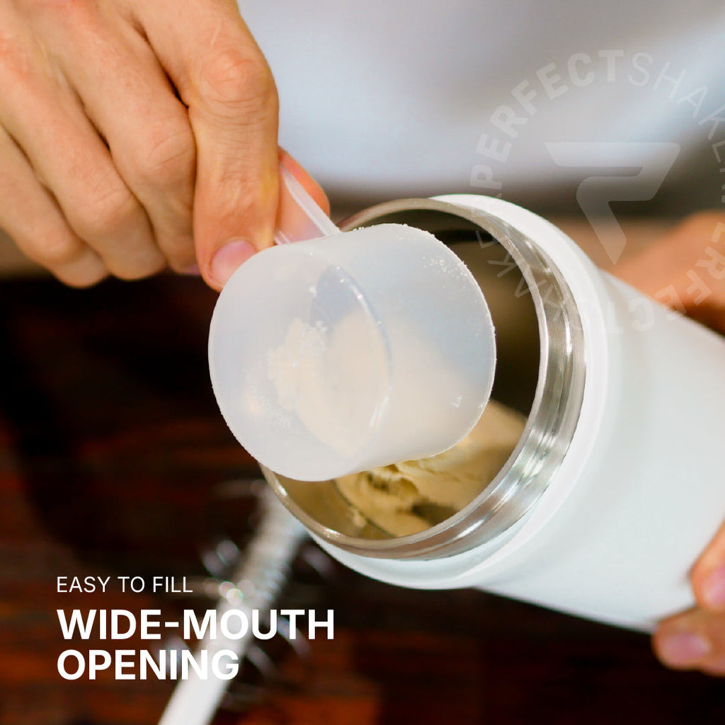 A close-up of a person's hands filling a white insulated tumbler with a scoop of powder through a wide, easy-to-reach mouth opening. White text in the lower left reads 'EASY TO FILL WIDE-MOUTH OPENING'.
