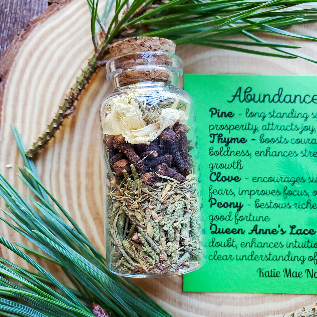 Glass jar with dried herbs on a wooden surface with green text card. Abundance Spell Bottle, Intention Setting Herbs for Prosperity and Sucess