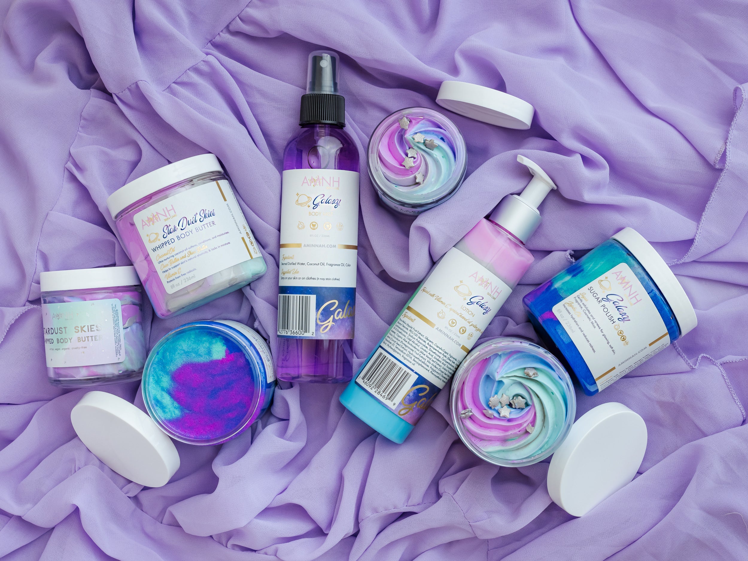 Collection of bath and body products on a purple fabric background. Mermaid Kisses Sugar Scrub bath and body collection featuring natural sugar scrubs, body butter, body lotion, and body mist on a soft purple fabric background. Clean beauty, cruelty-free, vegan skincare made with natural ingredients by a female-owned brand for smooth, hydrated, glowing skin.