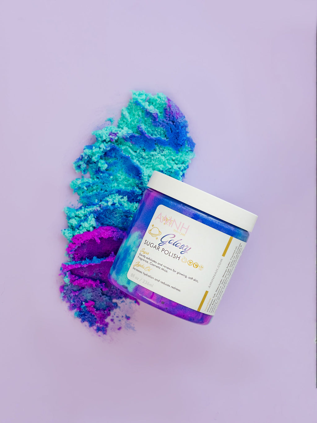 AMINNAH Galaxy Sugar Scrub in a jar with vibrant blue and purple sugar crystals on a lavender background. Clean beauty, cruelty-free, vegan body scrub made with natural ingredients to gently exfoliate, hydrate, smooth, and reveal glowing skin. Female-owned brand available at Tree of Life Grocers.