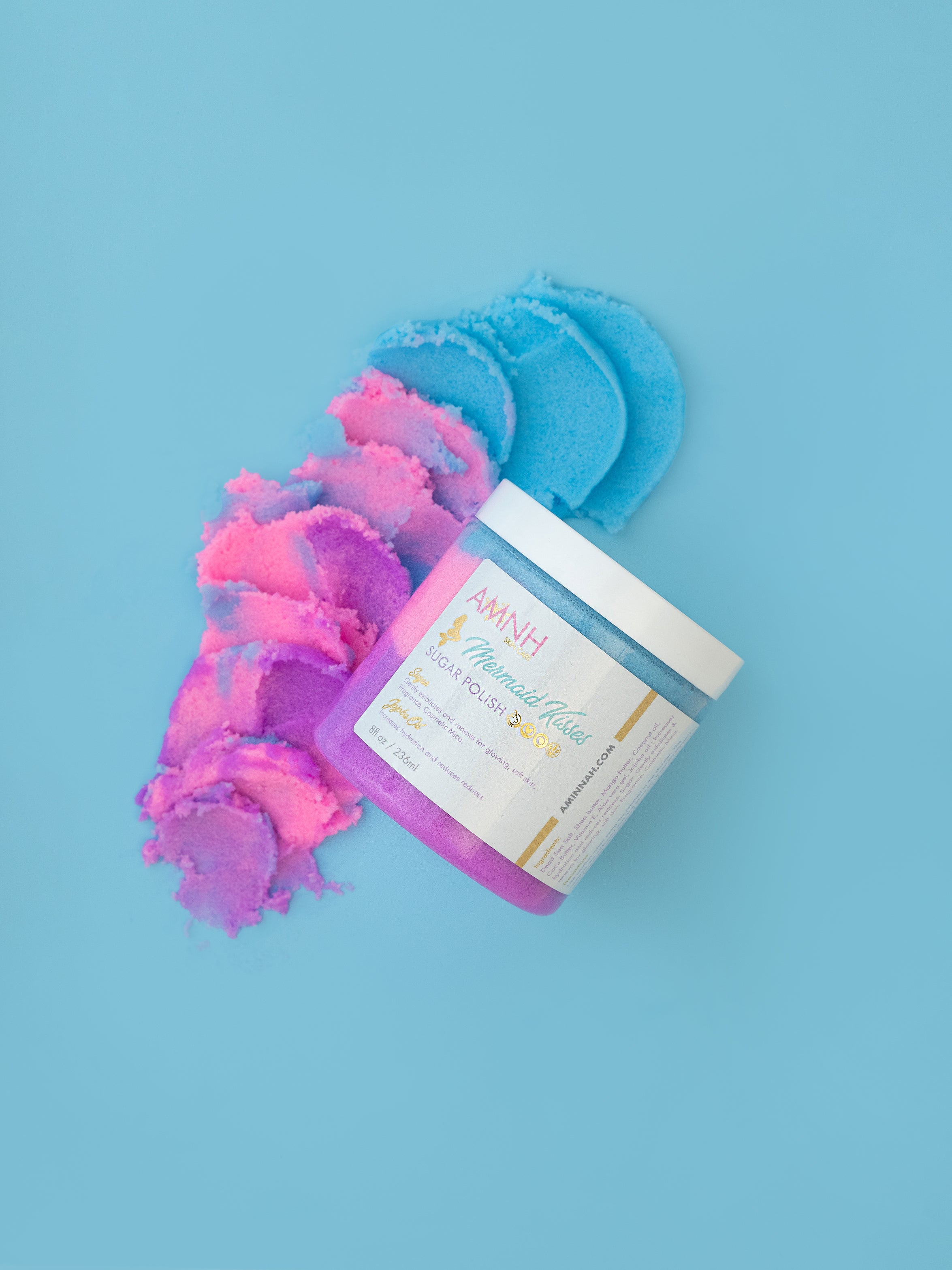 Mermaid Kisses Sugar Scrub with pink, purple, and blue natural sugar scrub beside an open jar on a light blue background. Clean beauty, cruelty-free, vegan body exfoliator made with natural ingredients by a female-owned brand for soft, glowing skin.