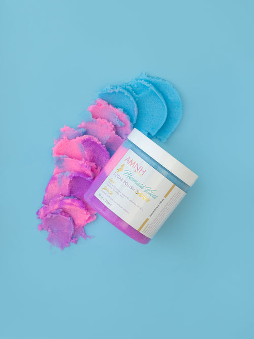 Mermaid Kisses Sugar Scrub with pink, purple, and blue natural sugar scrub beside an open jar on a light blue background. Clean beauty, cruelty-free, vegan body exfoliator made with natural ingredients by a female-owned brand for soft, glowing skin.
