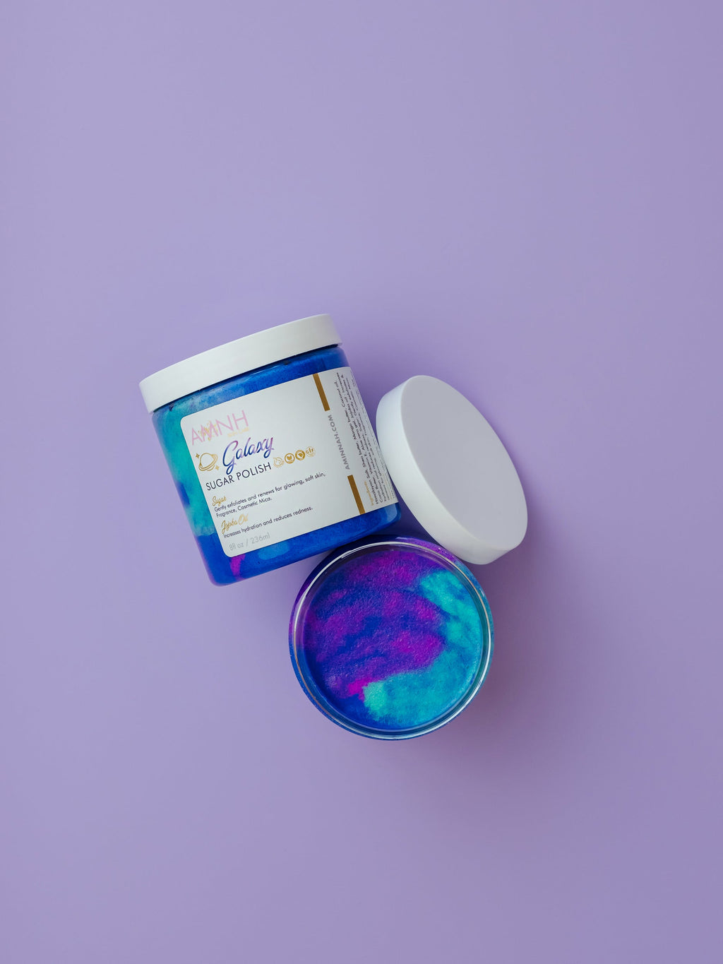 AMINNAH Galaxy Sugar Scrub in a jar with vibrant blue and purple sugar crystals on a lavender background. Clean beauty, cruelty-free, vegan body scrub made with natural ingredients to gently exfoliate, hydrate, smooth, and reveal glowing skin. Female-owned brand available at Tree of Life Grocers.