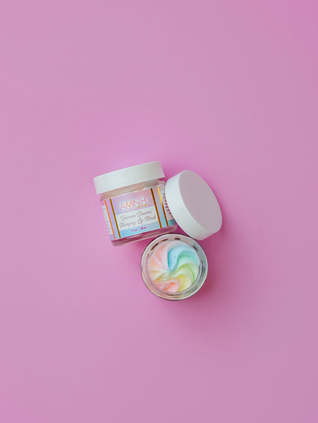 AMINNAH Birthday Cake Lip Scrub in a glass jar with whipped rainbow lip scrub on a pink background. Vegan lip exfoliator made with natural ingredients to gently buff away dry skin for soft, smooth lips. Clean beauty, cruelty-free lip care from a female-owned brand, perfect for nourishing, hydrating, and everyday self-care.