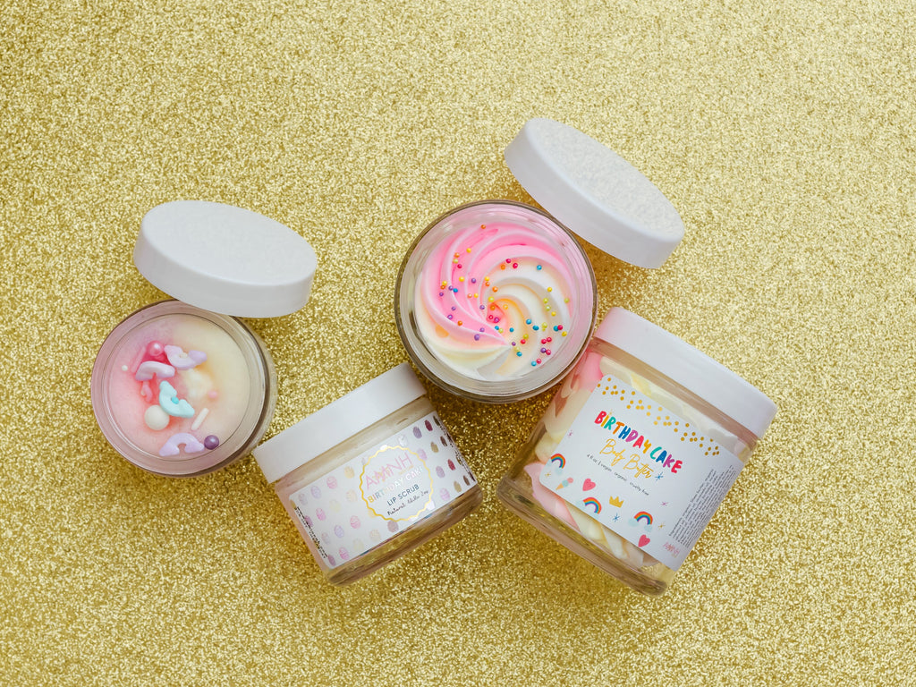 AMINNAH Birthday Cake skincare collection featuring Whipped Body Butter and Lip Scrub displayed on a gold background with open jars showcasing creamy pink and white whipped textures. Clean Beauty skincare made with natural ingredients, cruelty-free, vegan, female-owned brand proudly made in the USA, available at Tree of Life Grocers.