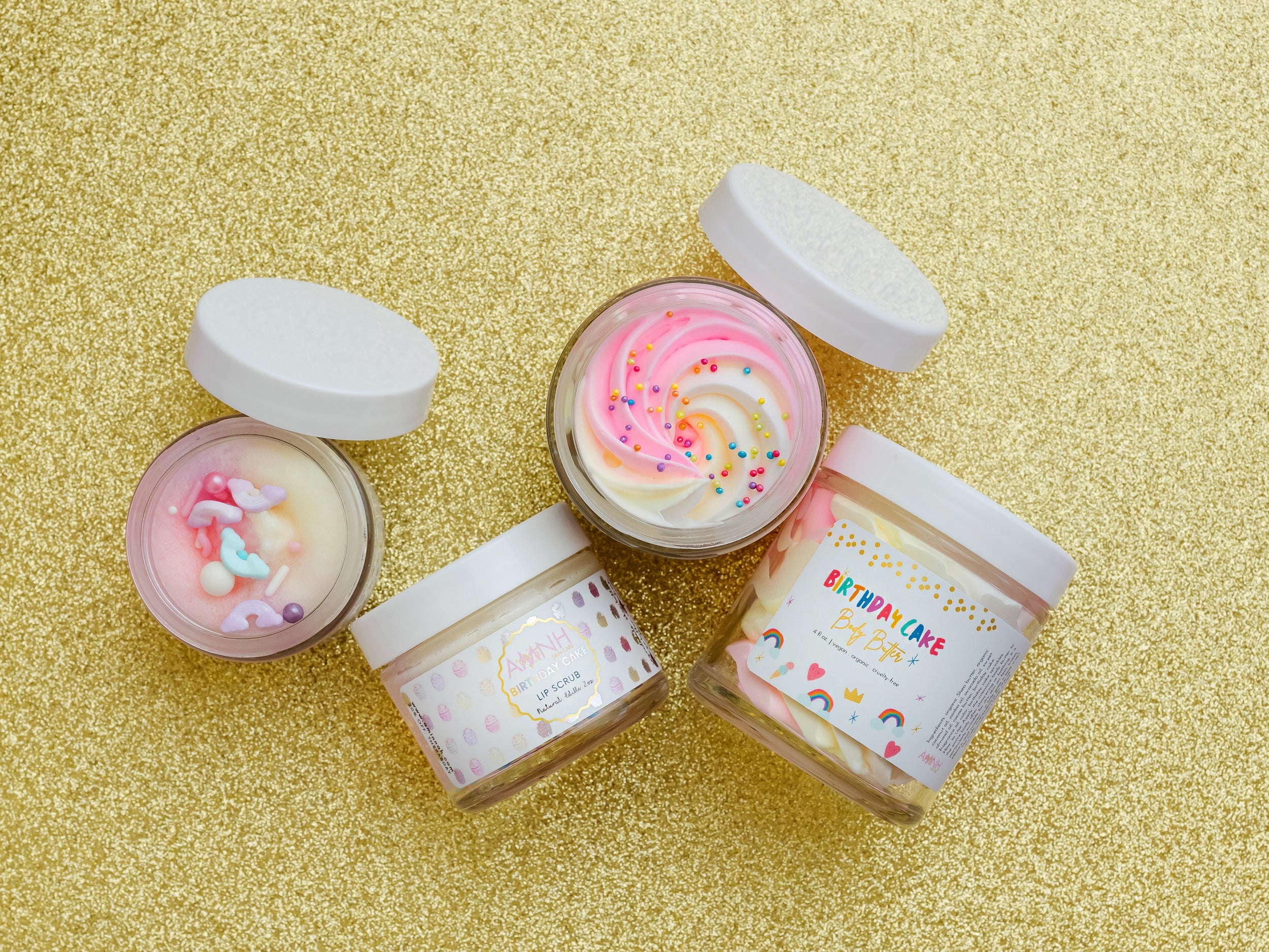 AMINNAH Birthday Cake skincare collection featuring Whipped Body Butter and Lip Scrub displayed on a gold background with open jars showcasing creamy pink and white whipped textures. Clean Beauty skincare made with natural ingredients, cruelty-free, vegan, female-owned brand proudly made in the USA, available at Tree of Life Grocers.