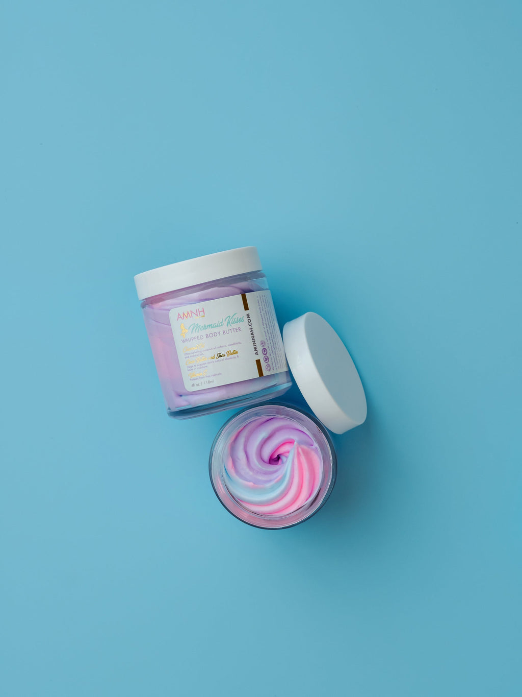 "Mermaid Kisses" Whipped Body Butter in a luxurious jar with fluffy pastel whipped body butter on a soft blue background. Clean beauty skincare made with natural ingredients that deeply moisturize and nourish skin. Cruelty-free, vegan, paraben-free, and gluten-free formula from a female-owned brand with recyclable packaging for healthy, silky-smooth, radiant skin.