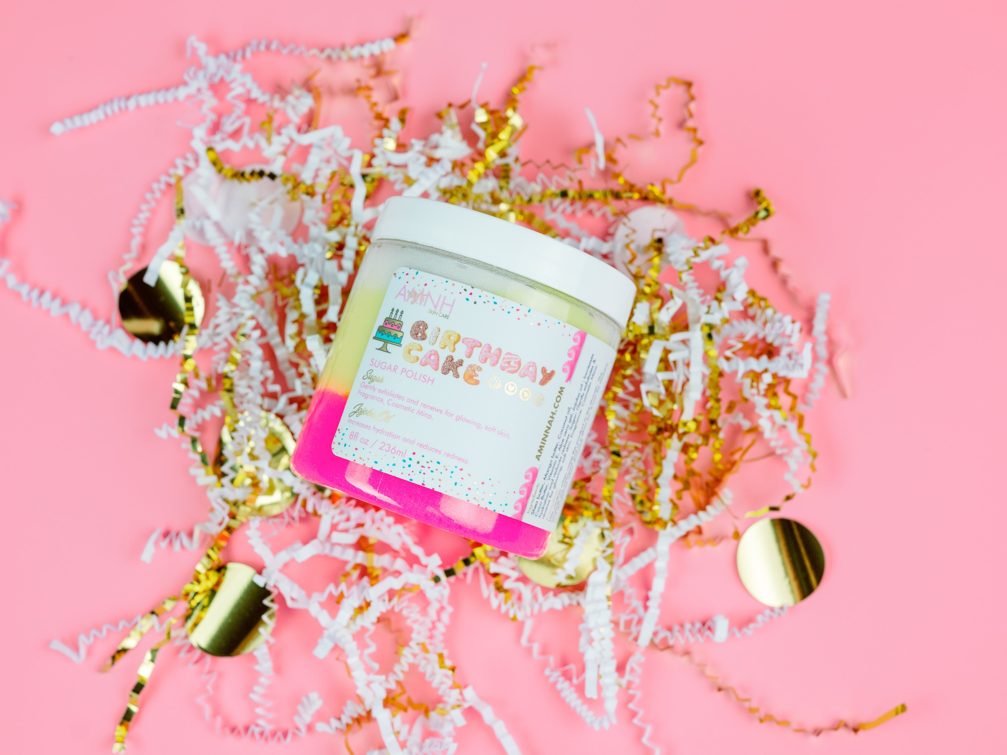 Birthday Cake Sugar Scrub in reusable jar on a pink background with festive gold and white confetti. Clean beauty, cruelty-free, vegan sugar scrub made with natural ingredients by a female-owned brand for gentle exfoliation, deep hydration, and glowing, silky-soft skin.