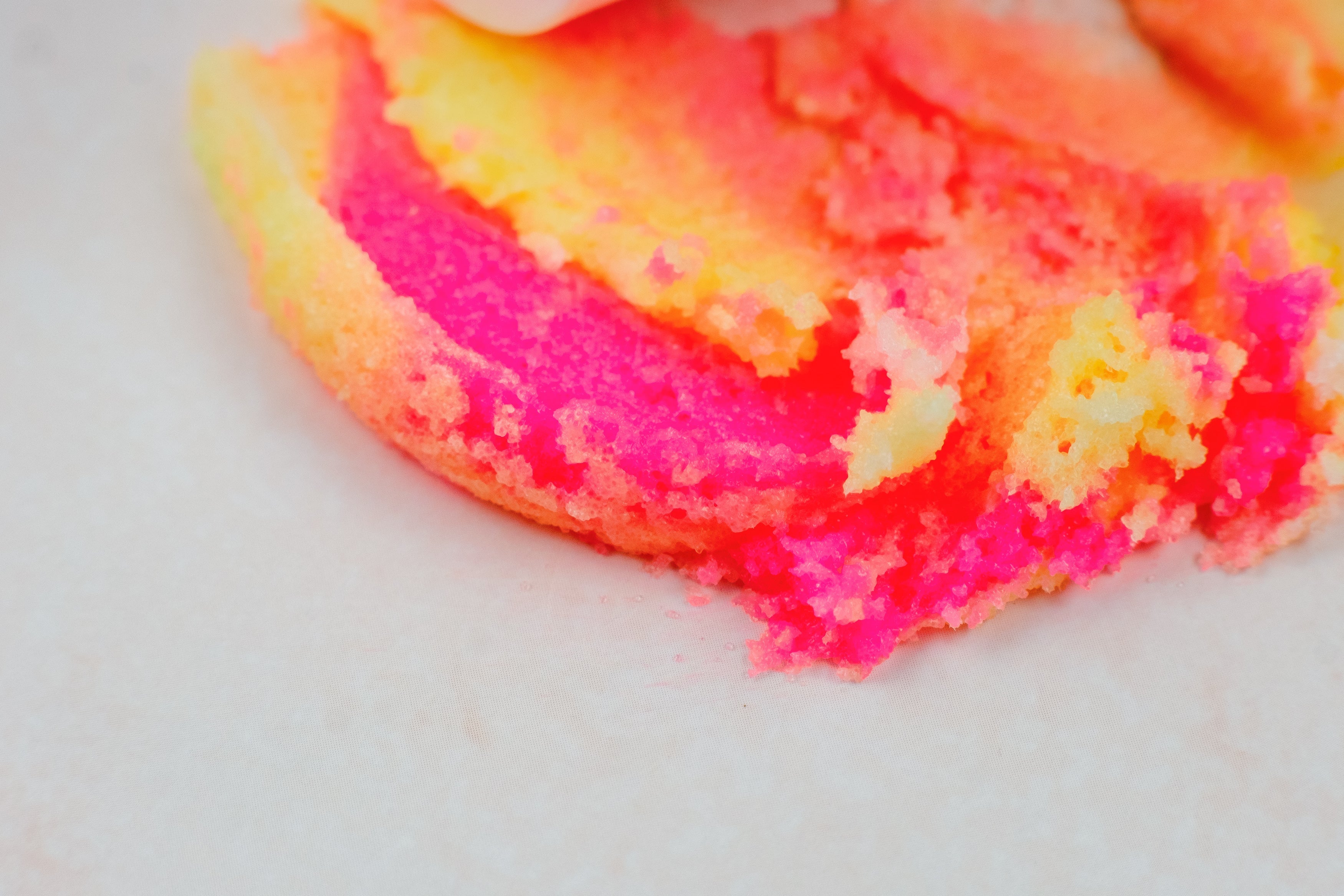 Birthday Cake Sugar Scrub close-up with vibrant pink, yellow, and orange swirls on a white background. This clean beauty, cruelty-free, vegan sugar scrub is handcrafted with natural ingredients by a female-owned brand to gently exfoliate, nourish, and leave skin soft, smooth, hydrated, and glowing with a delicious birthday cake-inspired scent.
