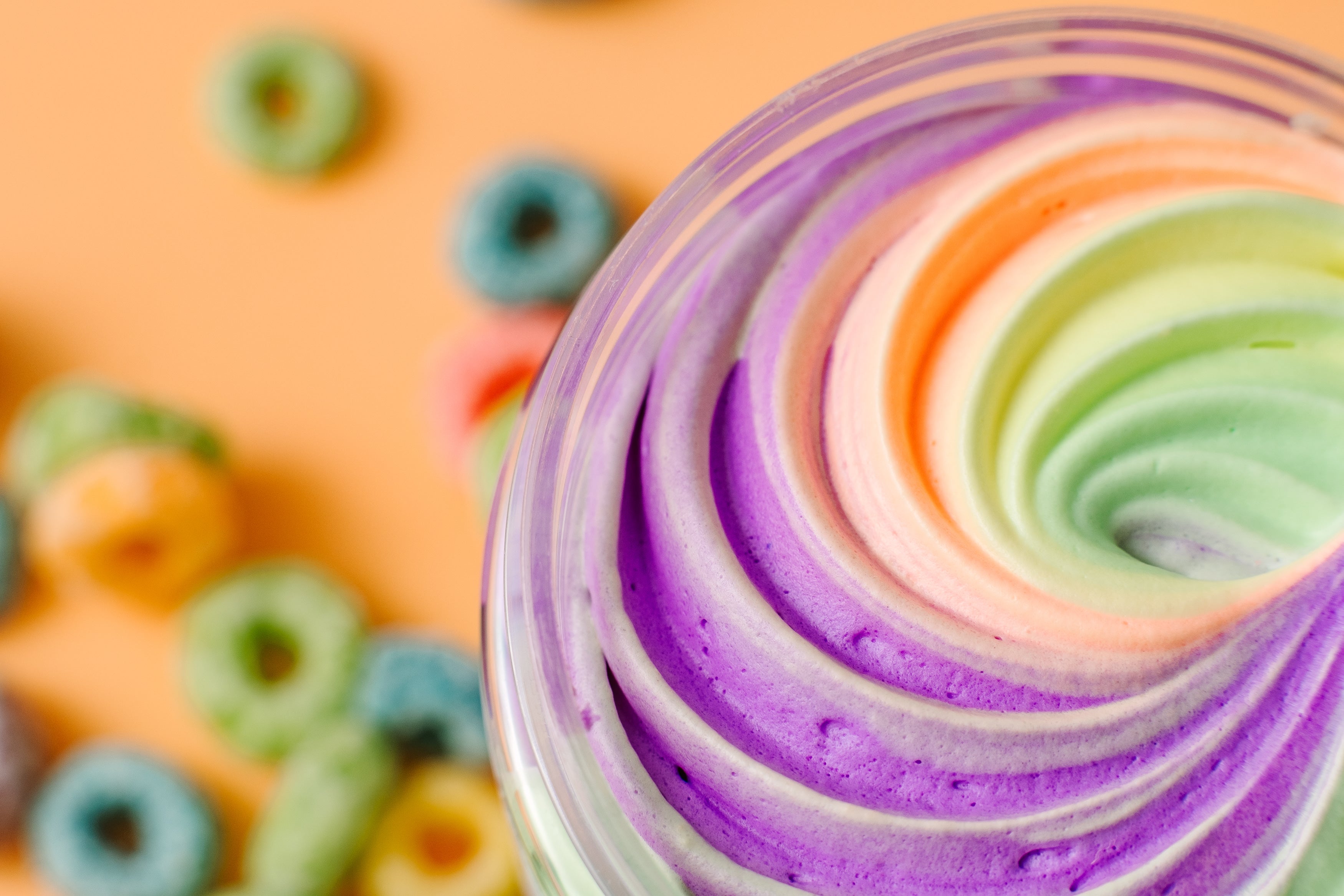 Close-up of AMINNAH FRUITY PEBBLEZ Whipped Body Butter showcasing its colorful swirled whipped texture in shades of purple, peach, and green with fruity cereal pieces in the background. Rich body butter made with shea butter, mango butter, vitamin E, and essential oils to help moisturize, soften, and nourish skin. Clean Beauty, cruelty-free, vegan, made with natural ingredients, female-owned brand, made in the USA, available at Tree of Life Grocers.