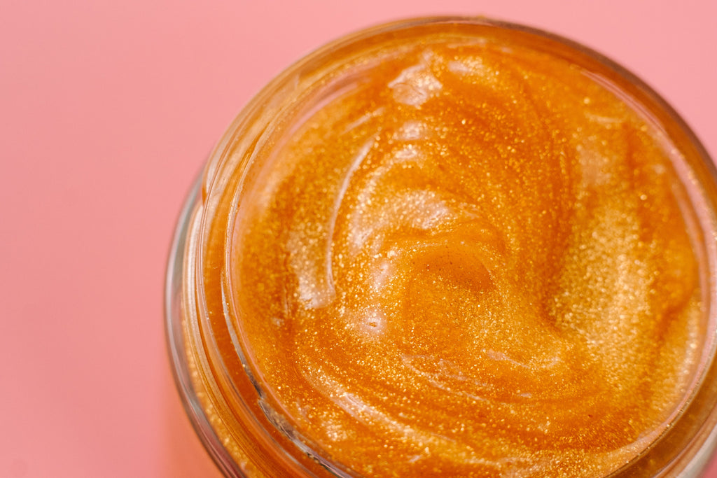 24K Golden Jelly Face Mask with luxurious shimmering gold jelly texture in an open glass jar. Clean beauty, cruelty-free, vegan skincare made with natural ingredients including aloe vera, aloe vera water, rose extract, vitamin E, coconut oil, 24K gold flakes, and golden jojoba beads. Female-owned brand formulated to deeply hydrate, lock in moisture, soothe, cool, tone, reduce inflammation, soften skin, support anti-aging, and promote a radiant, healthy, glowing complexion.