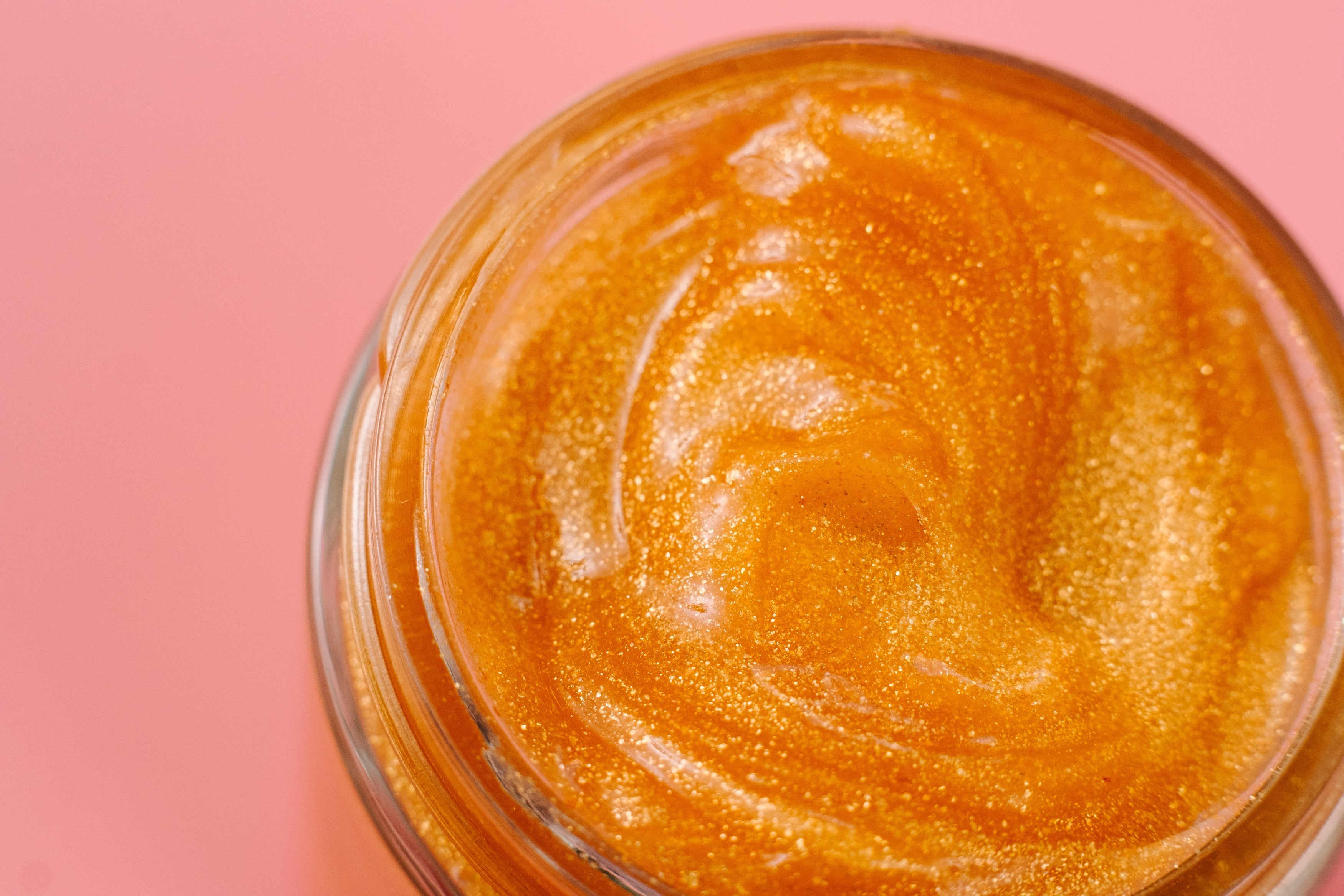 24K Golden Jelly Face Mask with luxurious shimmering gold jelly texture in an open glass jar. Clean beauty, cruelty-free, vegan skincare made with natural ingredients including aloe vera, aloe vera water, rose extract, vitamin E, coconut oil, 24K gold flakes, and golden jojoba beads. Female-owned brand formulated to deeply hydrate, lock in moisture, soothe, cool, tone, reduce inflammation, soften skin, support anti-aging, and promote a radiant, healthy, glowing complexion.