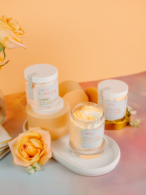 Candles with decorative packaging on a tray with flowers against a warm background. AMINNAH Peach Booty skincare collection featuring the Tightening & Lifting Scrub and Butt Butter displayed on an elegant tray with peach roses. Clean beauty, cruelty-free, vegan body care products made with natural ingredients from a female-owned brand for smooth, hydrated, firmer-looking skin.