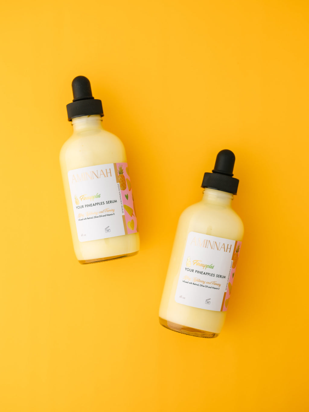 Two bottles of AMINNAH Fineapples Boob Serum displayed on a bright yellow background. This nourishing body and boob serum is formulated with pineapple fruit extract, retinol, vitamin E, argan oil, jojoba oil, rosehip oil, aloe vera, and botanical oils to hydrate, smooth, and soften skin. Clean beauty, cruelty-free, vegan, made with natural ingredients, and crafted by a female-owned brand for radiant, healthy-looking skin.