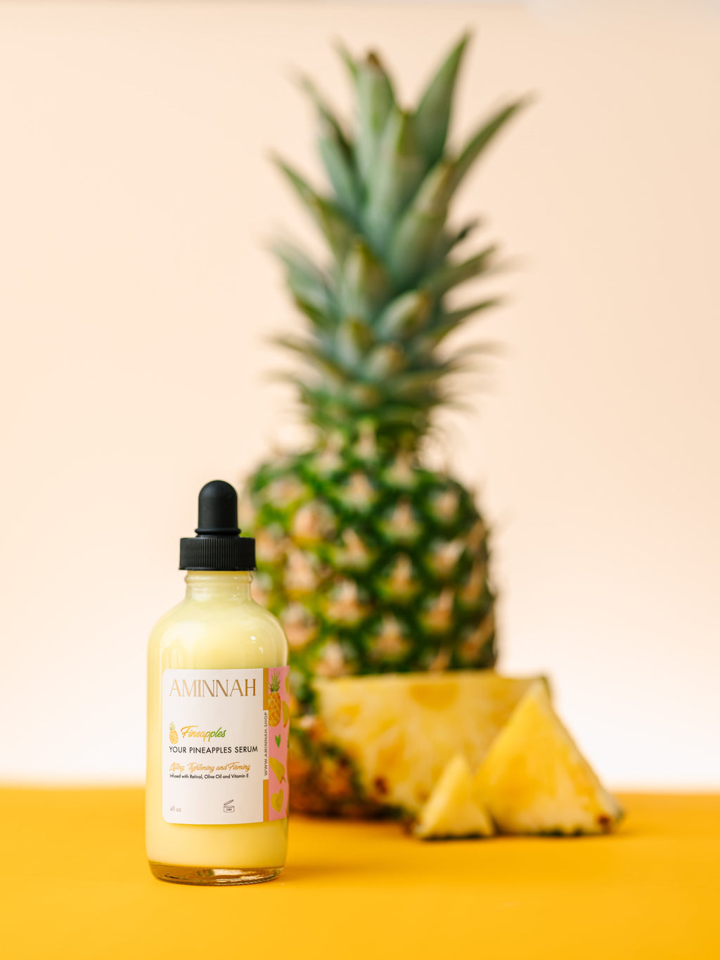 AMINNAH Fineapples Boob Serum bottle displayed in front of a fresh pineapple on a yellow background. Hydrating boob and body serum made with pineapple extract, retinol, vitamin E, argan oil, jojoba oil, rosehip oil, aloe vera, and botanical oils to nourish, smooth, and soften skin. Clean beauty, cruelty-free, vegan, made with natural ingredients, and crafted by a female-owned brand.