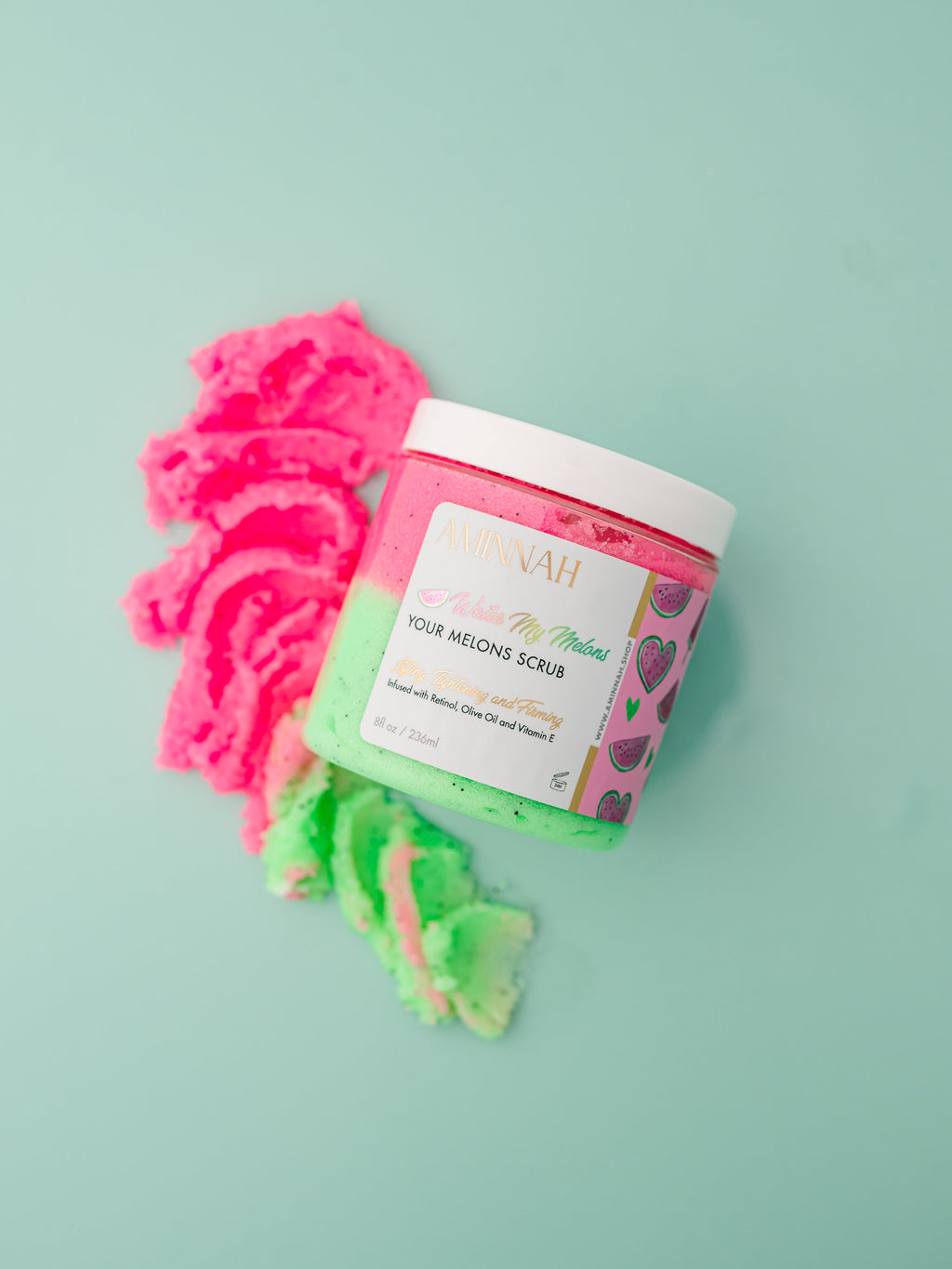 Jar of body scrub with pink and green scrubs on a light blue background. Water My Melons Boob Sugar Scrub in an open jar with exfoliating pink sugar scrub and branded container on a teal background. Clean beauty skincare made with natural ingredients including watermelon fruit extract, shea butter, cocoa butter, mango butter, aloe vera, vitamin E, retinol, and botanical oils. Cruelty-free, vegan, female-owned beauty brand.