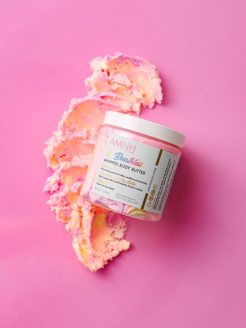 AMINNAH "Breathless" Whipped Body Butter in an 8 oz jar on a pink background with whipped body butter texture, made with natural ingredients including organic shea butter, cocoa butter, mango butter, coconut oil, jojoba oil, and vitamin E. Clean beauty moisturizer that is vegan, cruelty free, paraben free, gluten free, from a female-owned brand for soft, nourished, deeply hydrated skin.