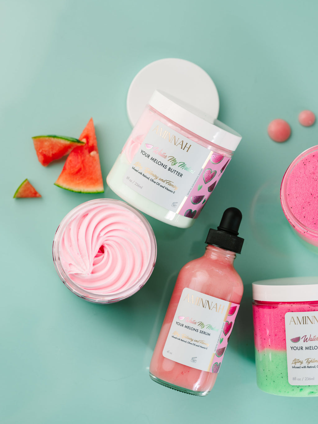 Watermelon skincare collection featuring AMINNAH 'Water My Melons' Boob Serum, body butter and exfoliating scrub with fresh watermelon slices on a mint green background. Hydrating breast serum with natural ingredients, vegan, cruelty-free, clean beauty, female-owned skincare brand. Anti-Aging serum for soft, nourished skin. Clean beauty, cruelty-free skincare from a female-owned brand. Vegan formula made with skin-loving botanical ingredients for daily hydration.