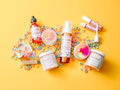 Assorted beauty products including bottles, jars, and a lip balm on a yellow background. AMINNAH "FRUT LOOPS" Body Care Bundle displayed with whipped body butter, sugar scrub, body oil, lip gloss, and handcrafted soap on a bright yellow background surrounded by colorful cereal pieces. Clean beauty, cruelty-free, vegan, femae-owned, skincare collection made with naturally derived ingredients including shea butter, coconut oil, jojoba oil, avocado oil, cocoa butter, rosehip oil, vitamins C and E
