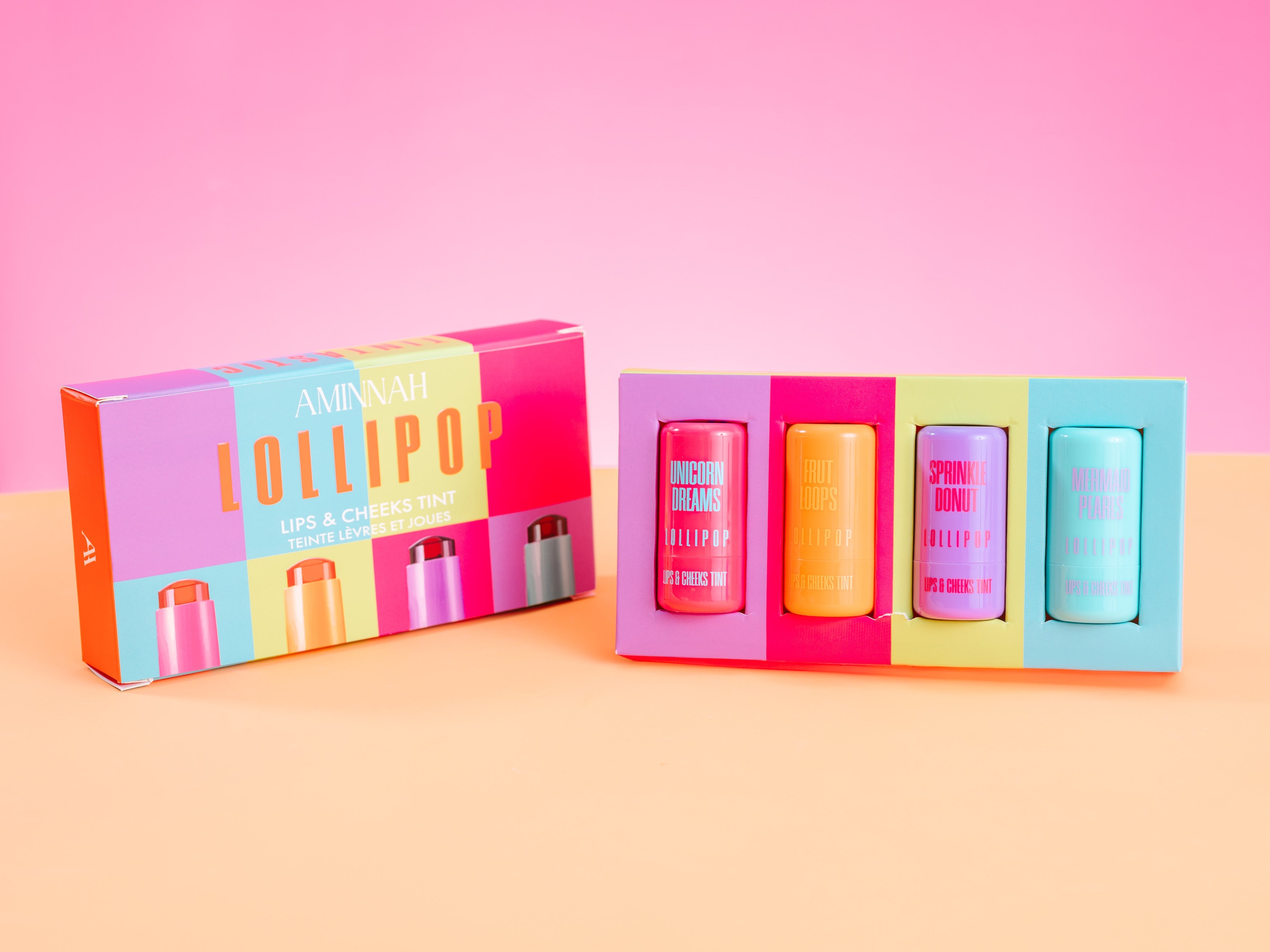 Colorful lip balm set with packaging on a pink and orange background. AMINNAH LOLLIPOP Lips & Cheeks Tints Gift Set featuring four vibrant lip and cheek tints made with Aloe Vera, Niacinamide, Hyaluronic Acid, and Goji Berry. Vegan, cruelty-free clean beauty from a female-owned brand.