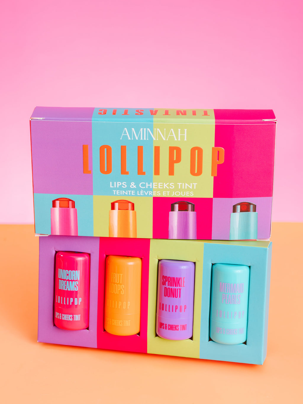 Set of lip and cheek tint bottles in a colorful box with 'Aminah Lollipop' branding on a pink and orange background. AMINNAH LOLLIPOP Lips & Cheeks Tints Gift Set showcasing four vibrant hydrating lip and cheek tints in colorful gift box packaging. Made with Aloe Vera, Hyaluronic Acid, Niacinamide, and Goji Berry. Vegan, cruelty-free clean beauty from a female-owned brand with skin-loving ingredients.