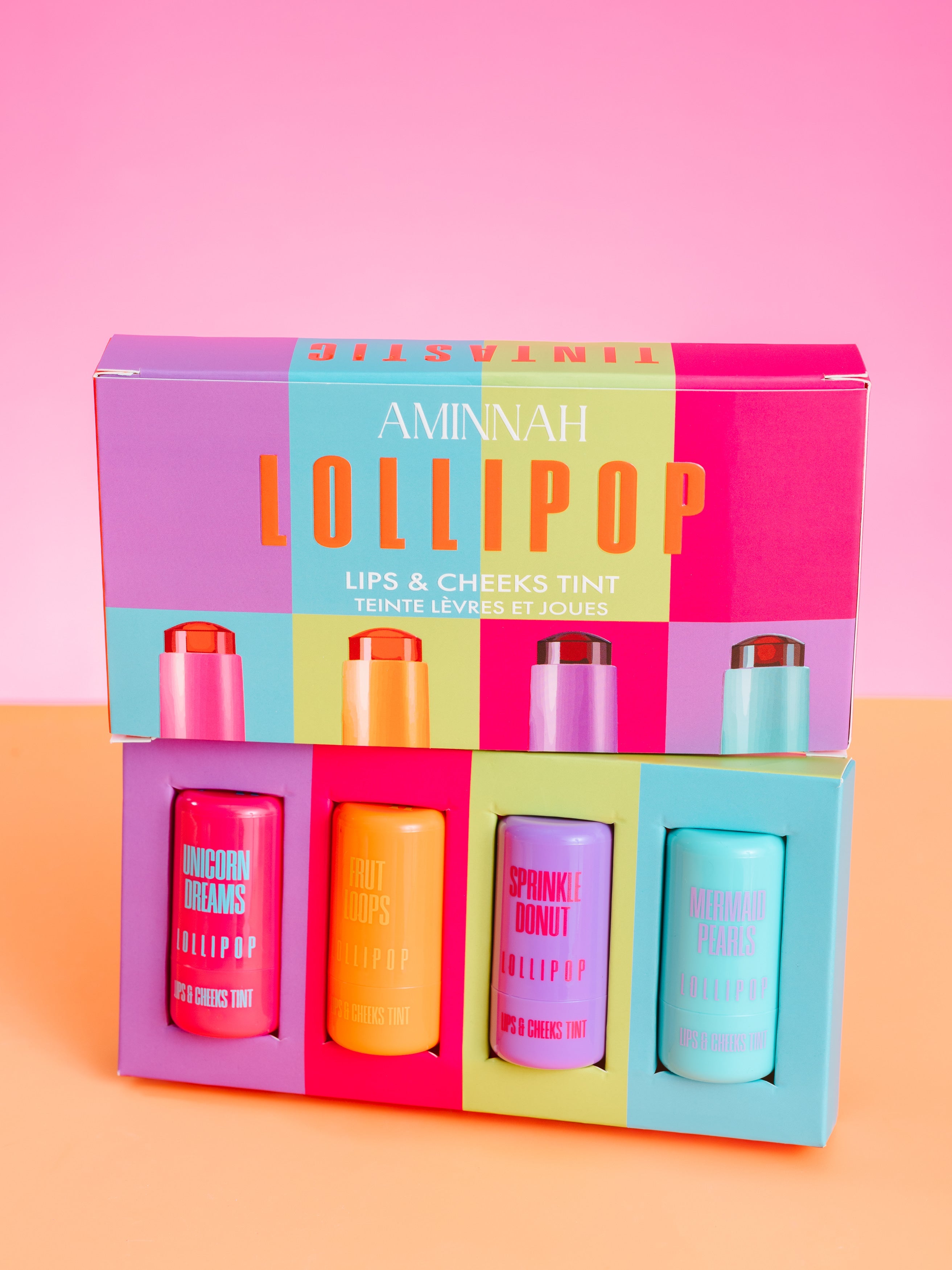 Set of lip and cheek tint bottles in a colorful box with 'Aminah Lollipop' branding on a pink and orange background. AMINNAH LOLLIPOP Lips & Cheeks Tints Gift Set showcasing four vibrant hydrating lip and cheek tints in colorful gift box packaging. Made with Aloe Vera, Hyaluronic Acid, Niacinamide, and Goji Berry. Vegan, cruelty-free clean beauty from a female-owned brand with skin-loving ingredients.