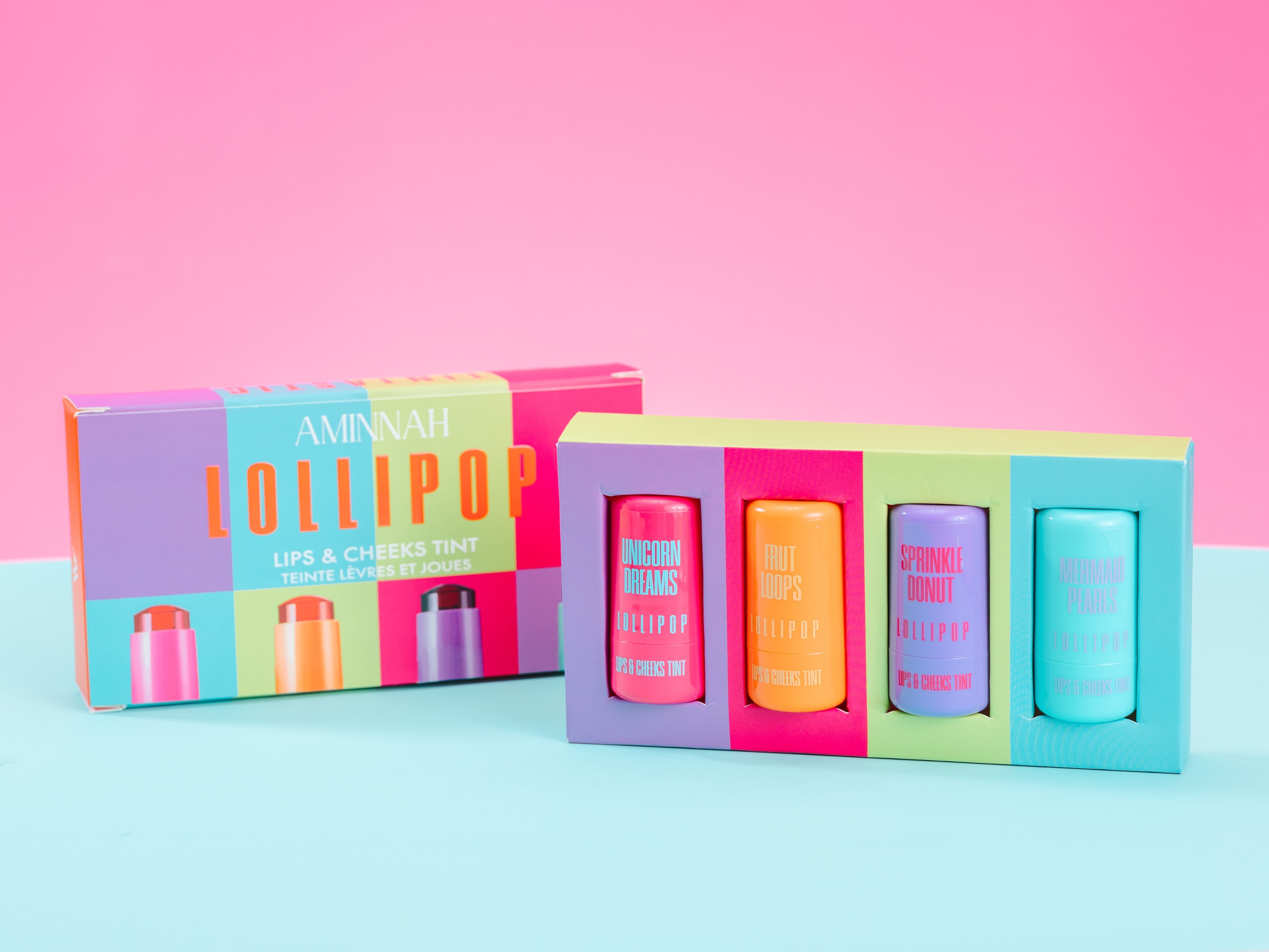 Colorful lip balm set with packaging on a pink and blue gradient background.  Open AMINNAH LOLLIPOP Lips & Cheeks Tints Gift Set featuring four hydrating lip and cheek tints. Vegan, cruelty-free clean beauty with Aloe Vera, Hyaluronic Acid, Niacinamide, and Goji Berry from a female-owned brand.