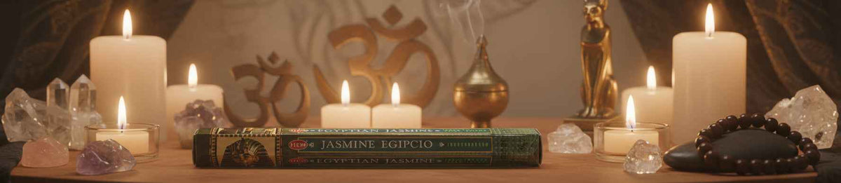 A book titled 'JASMINÉ ESPRIT SUISSE' lies on a wooden surface surrounded by lit white pillar candles, crystals, a small gold figurine, and a black beaded mala, with a warm, mystical background.
