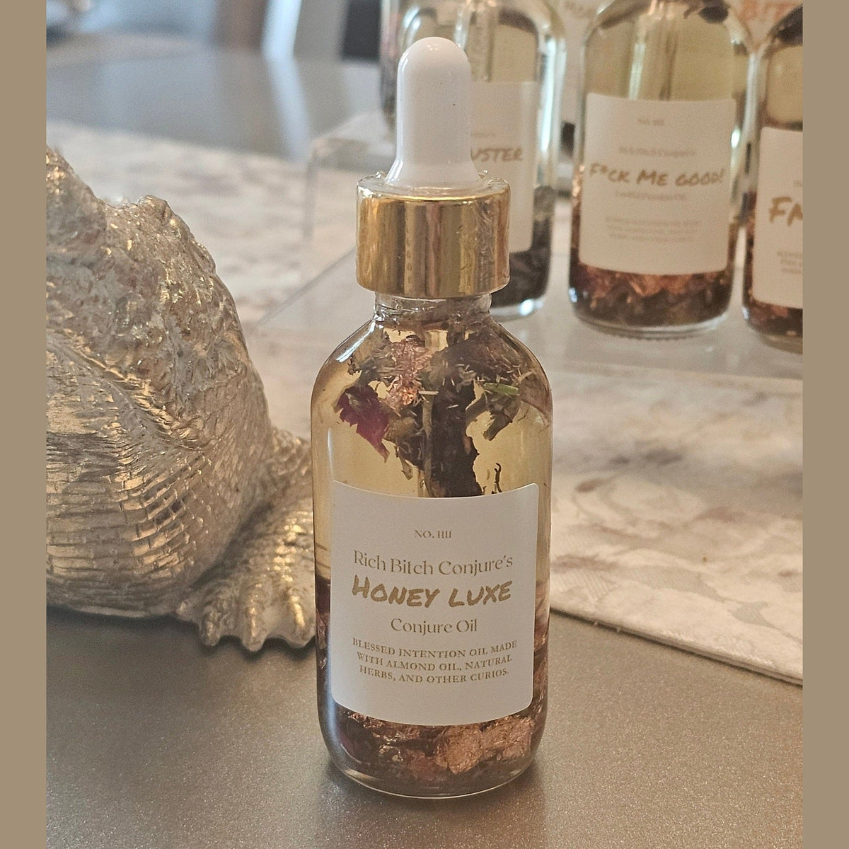 Bottle of 'Honey Luxe' conjure oil with a dropper on a surface.
