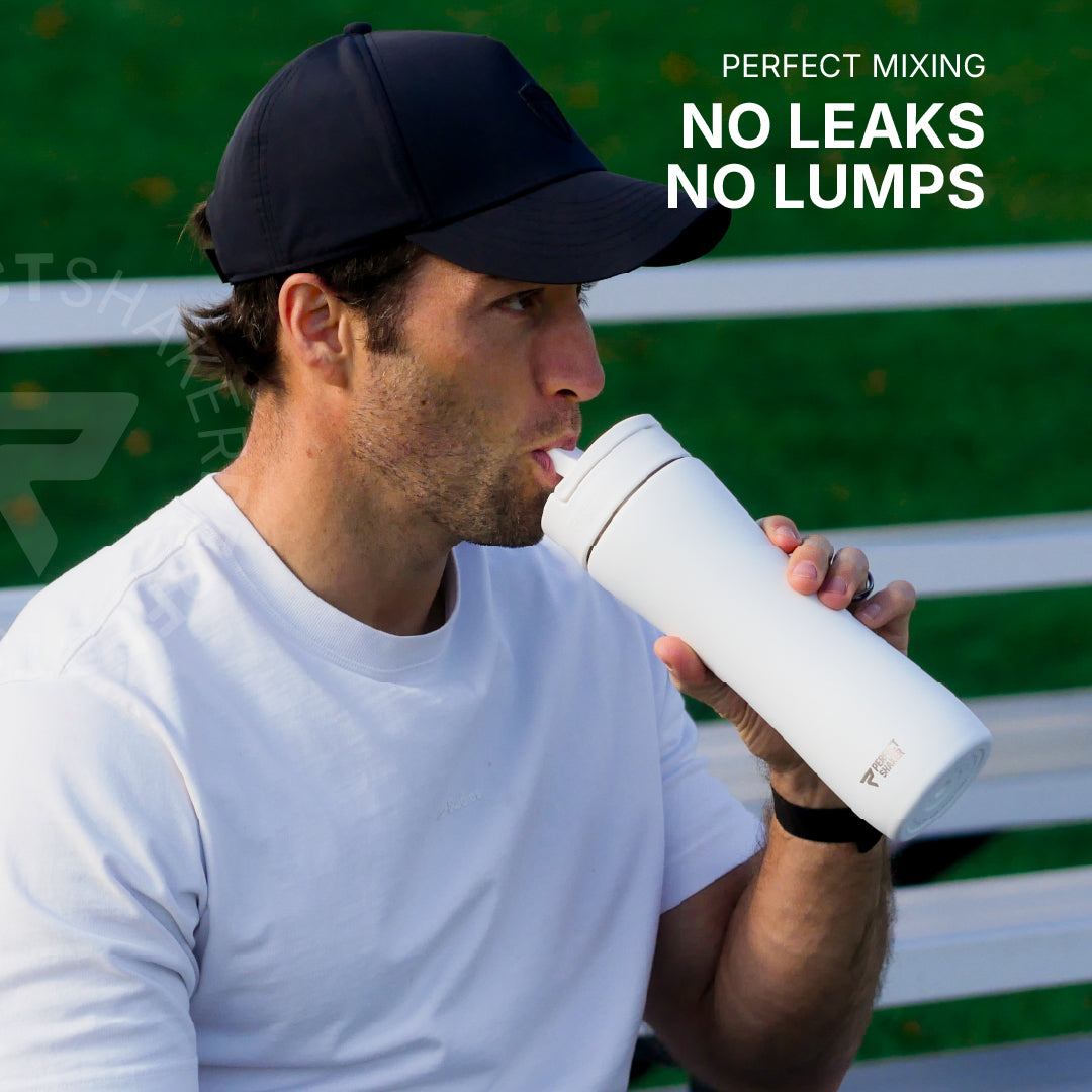 A man wearing a black baseball cap and white t-shirt drinking from a white insulated water bottle. The background shows a green outdoor setting with white bench slats, and text on the top right reads 'PERFECT MIXING NO LEAKS NO LUMPS'.