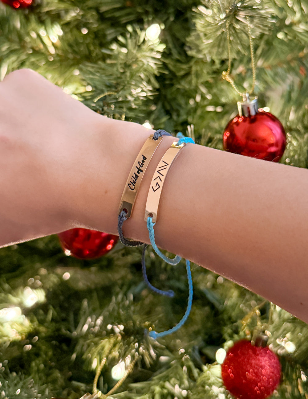 A stylish wrist featuring multiple bracelets, including the Black Child of God string bracelet, elegantly styled against the festive background of a glowing Christmas tree.