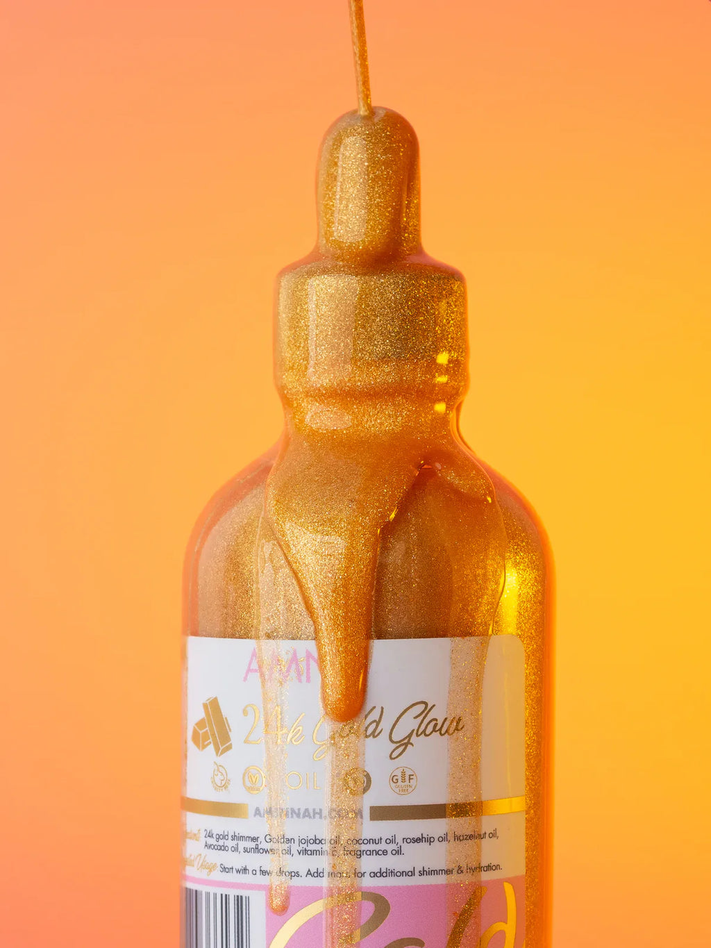 24K Gold Glow Body Oil bottle with shimmering golden oil dripping from the dropper against a warm golden background. Luxurious body oil made with natural ingredients to nourish, hydrate, and illuminate skin. Clean beauty, cruelty-free, vegan skincare from a female-owned brand for a radiant, healthy-looking glow.