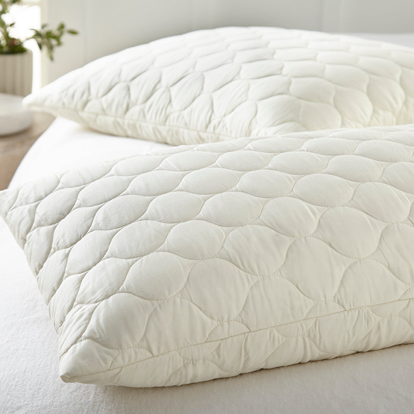 Quilted white comforter on a bed with pillows in a bright room. Organic Cotton Quilted Pillow Protectors