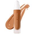 Fenty Beauty Pro Filt'r Soft Matte Longwear Liquid Foundation in a frosted glass bottle with a white pump, displayed in front of a smooth swipe of warm medium-brown foundation on a clean white background.