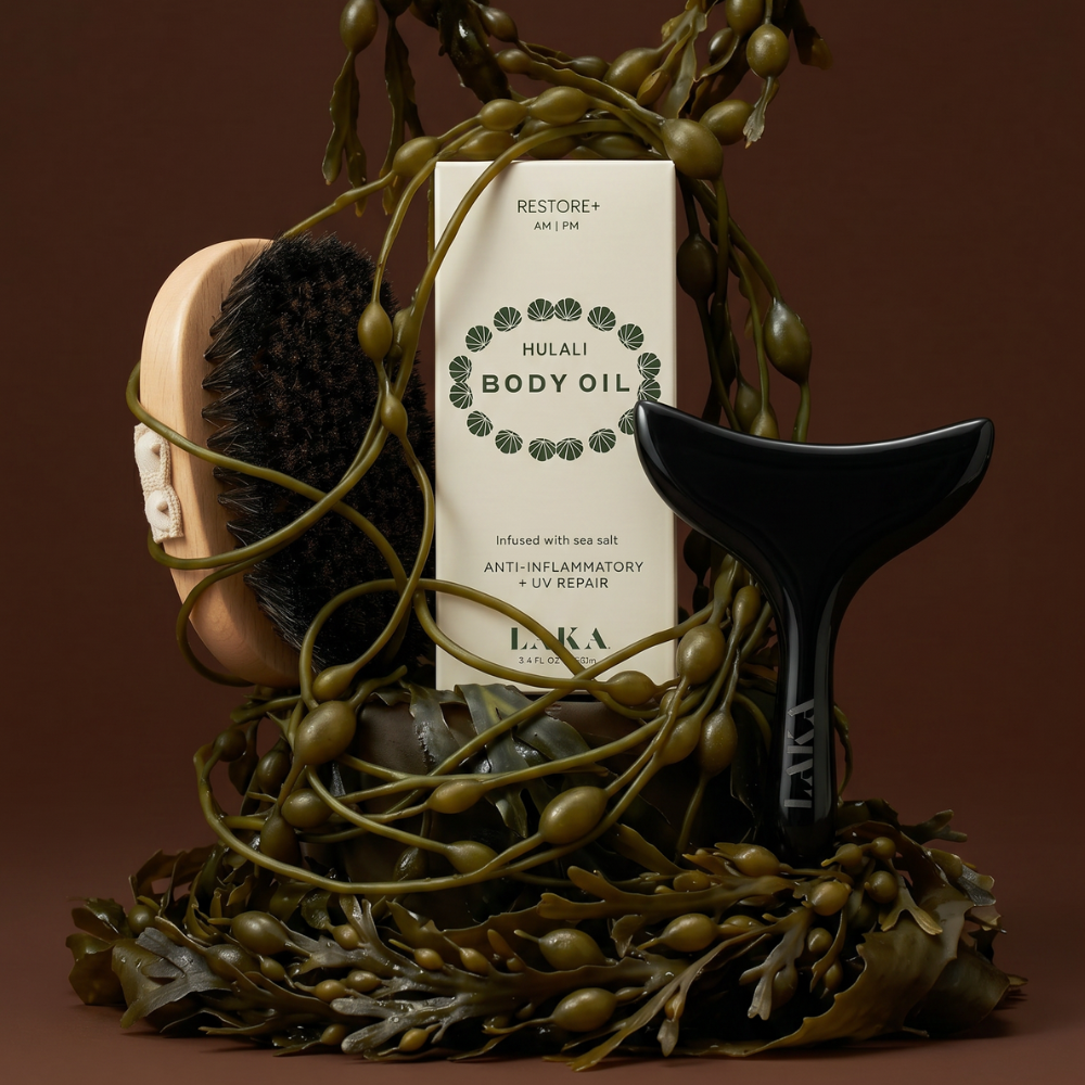 Hulali Body Oil bottle with a brush and leafy branches on a brown background