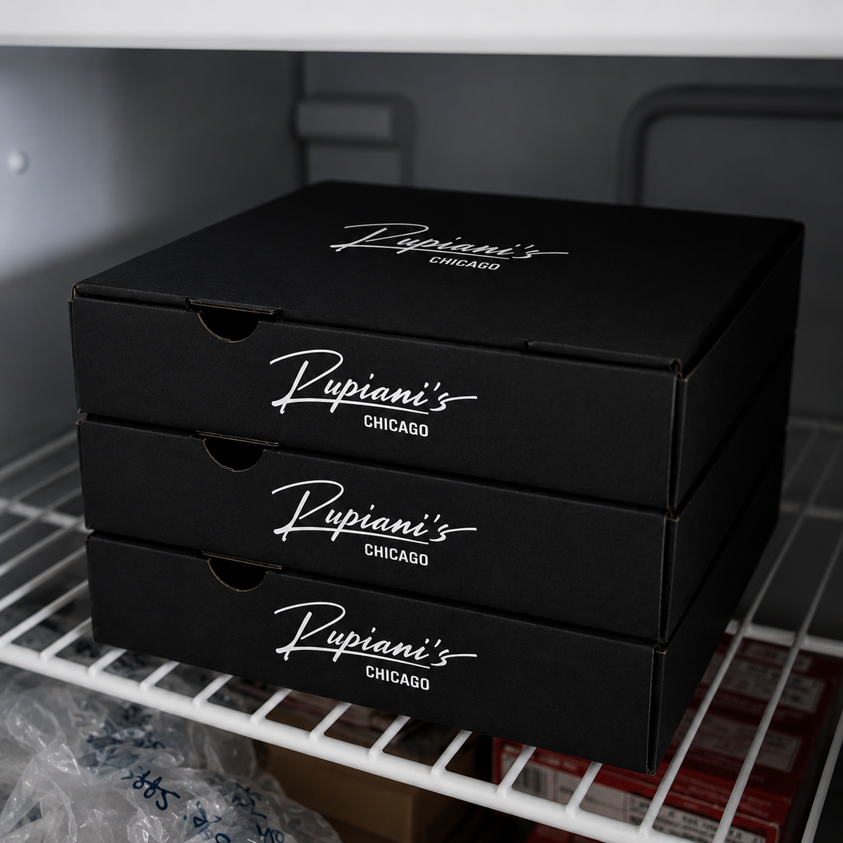 Stack of black Rupani's Chicago pizza boxes on a shelf.