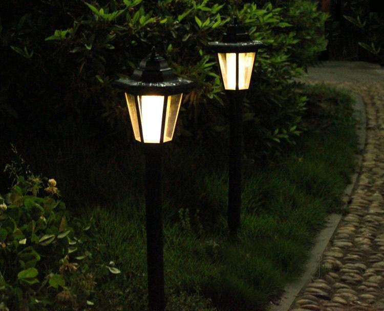 Two solar garden lights on a pathway surrounded by greenery at night.