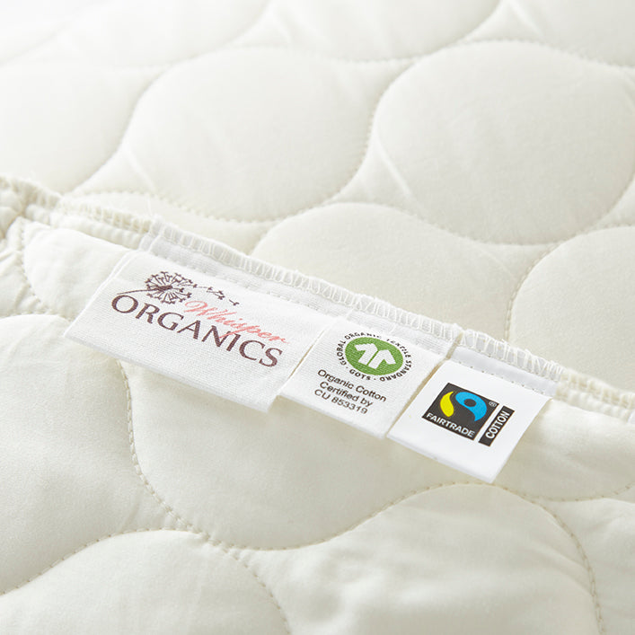 Close-up of a mattress pad with a label indicating organic and Fairtrade certification. Organic Cotton Quilted Pillow Protectors